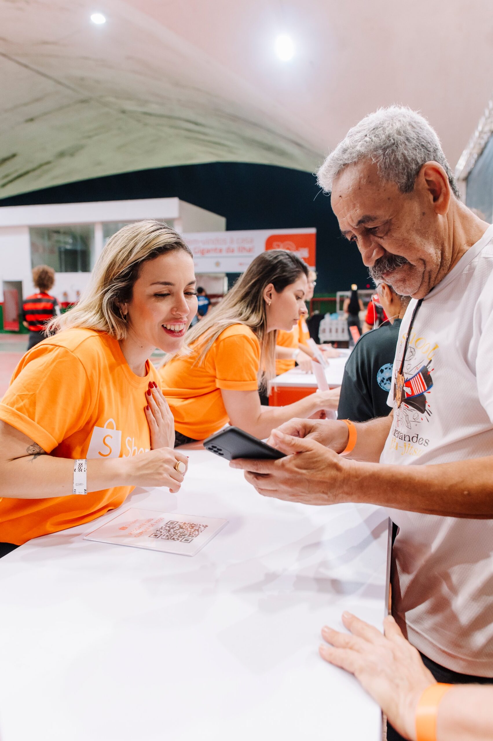 Promotora da Shopee orienta um torcedor a ler o QR code do cupom no celular, no balcão da ativação